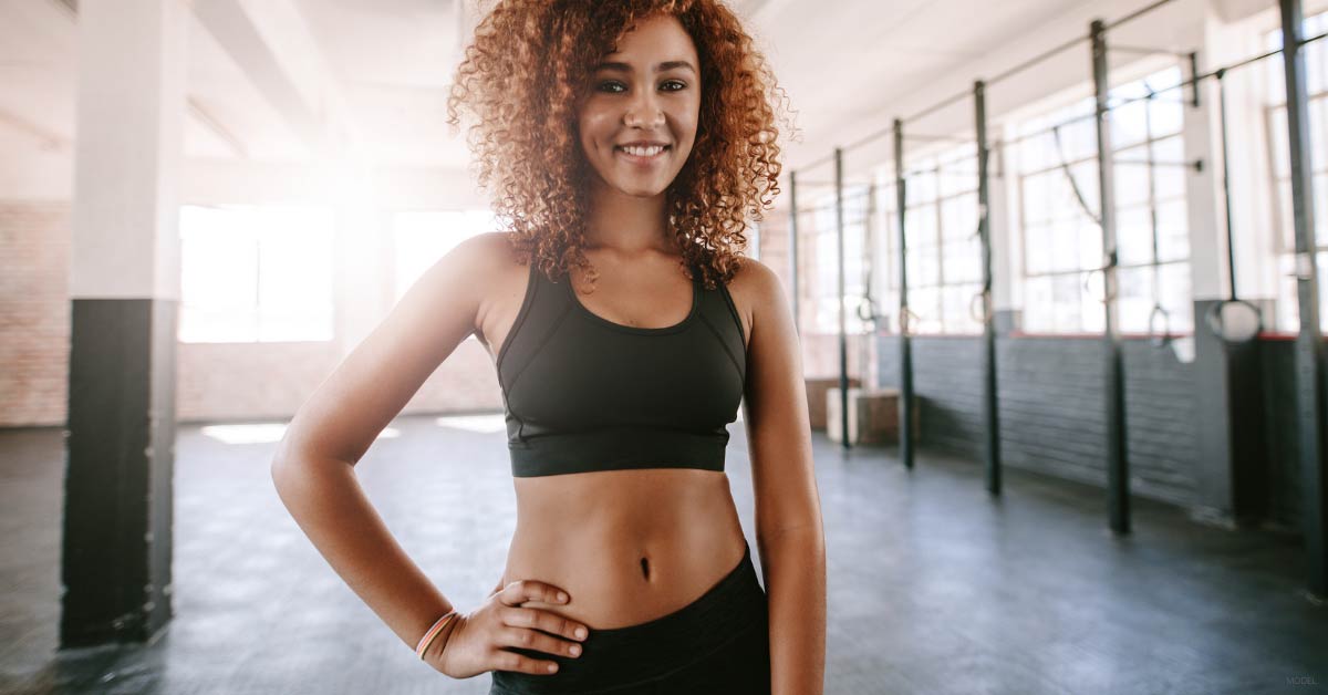 A woman poses at the gym and is happy with her tummy tuck results.