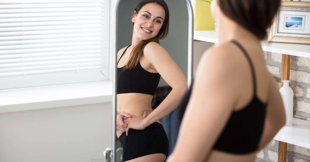 Woman looks in mirror at tummy tuck results