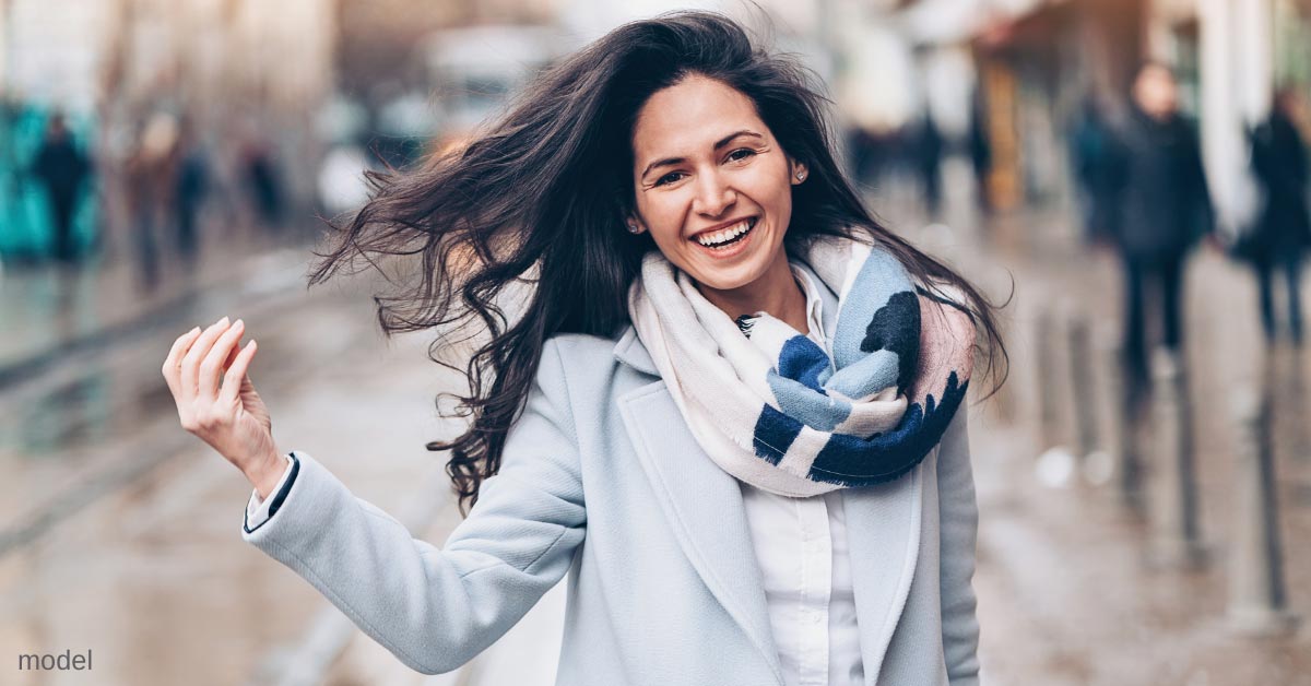 Woman in street smiling with hand held up touching hair (MODEL)