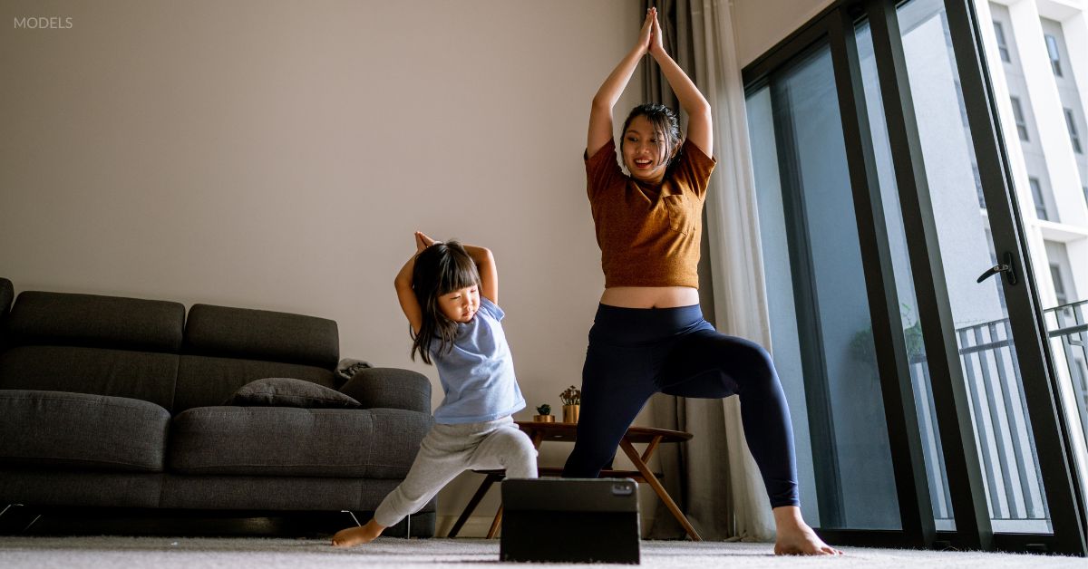 Woman and her daughter (models) doing yoga together in the living room.