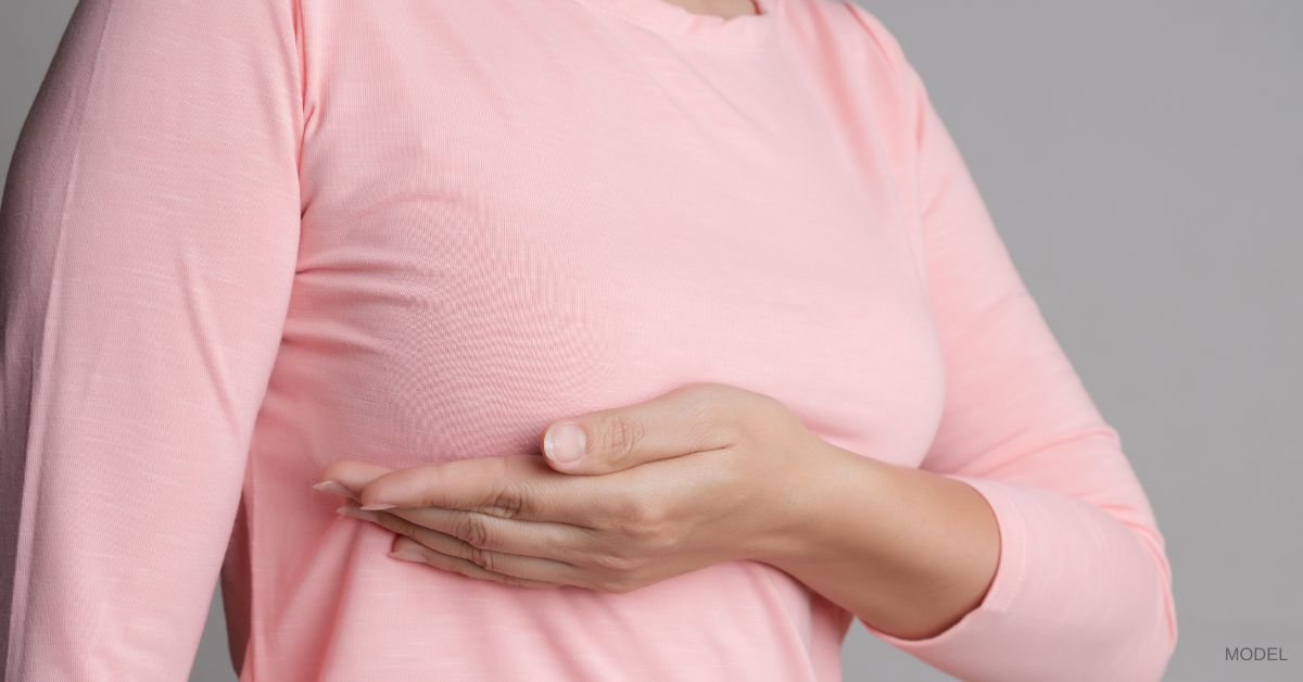 Woman holding her breasts from underneath (model) shown wearing a pink shirt.