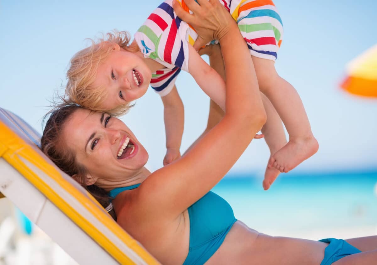 Mom smiling in bikini holding up baby at the beach after mommy makeover in Northbrook, IL
