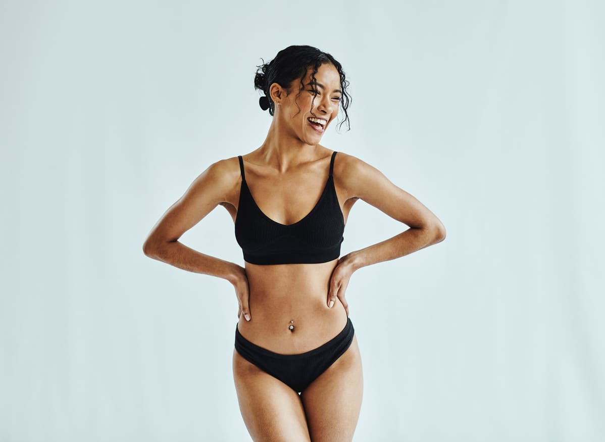 Smiling woman in black undergarments, representing confidence after breast reconstruction surgery.
